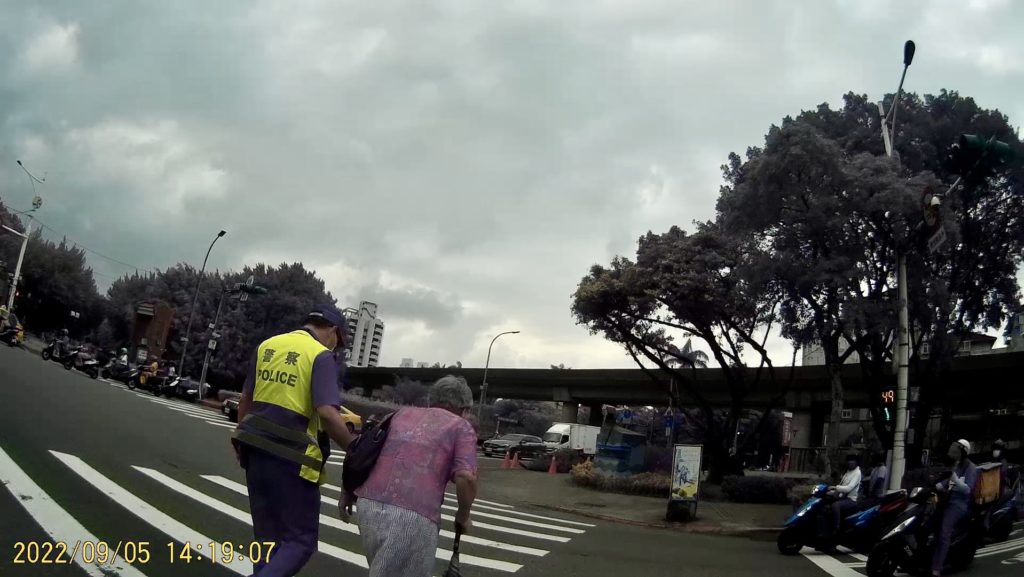 臺北市保安警察大隊吳中隊長迅速下車攙扶老婦人，等行人號誌綠燈後陪同過馬路至安全處。