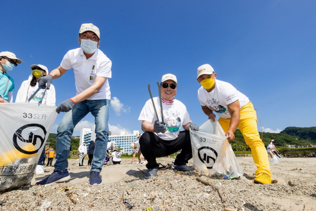 東森集團總裁王令麟（中）與副市長劉和然(左)率先拿起垃圾袋與夾子，撿拾沙灘上的廢棄物，在熊媽媽買菜網工作的更生人阿凱(右)也號召多位更生人一起參與淨灘。