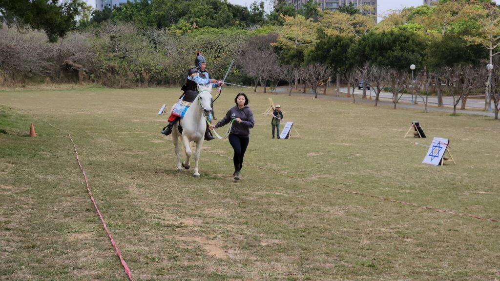 在東海湖旁大草地，台灣騎射大師鍾國華表演古裝騎兵射馬武藝，馬術社學生在旁協助。（圖/陳惠玲攝影）