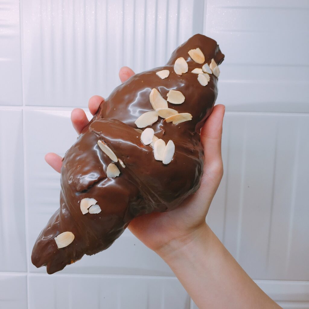 成人手掌般大的「巧克力牛角」，超過15公分的酥脆可頌裹上香濃巧克力醬和杏仁片，期間限定45元。（圖／普諾麵包坊．忠孝店提供）