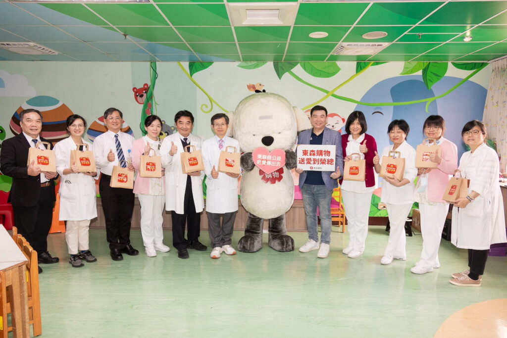 東森購物在兒童節前夕安排吉祥物「得意狗」至臺北榮總兒童病房送愛，由東森購物總經理彭鴻珷(右5)代表送孩子們兒童節禮物，臺北榮總副院長林永煬(左6)及兒童醫學部主任牛道明(左5)皆現身感謝這份溫暖心意。