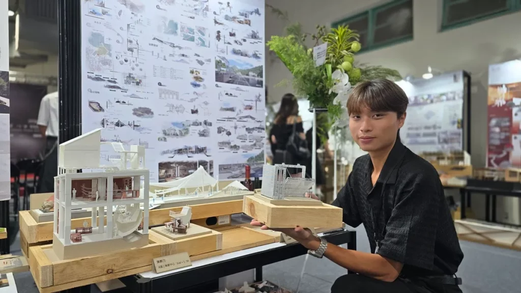 學生林峻民以作品〈漁創力〉翻轉漁港想像,他手持模型搶魚平台,說明當地下午5點漁船進港後「搶魚」的傳統商業特色,為此設計出可移動式的分流平台。這不僅能避免魚貨在拍賣過程中受損,更能讓遊客與居民擁有更優質的「搶魚體驗」。(圖/陳惠玲攝影)